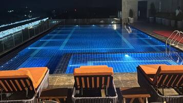 A rooftop pool area with lounge chairs and a view of the city at night.