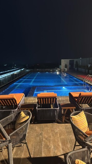 Un espace piscine aménagé sur le toit, avec des chaises longues et une vue sur la ville la nuit.