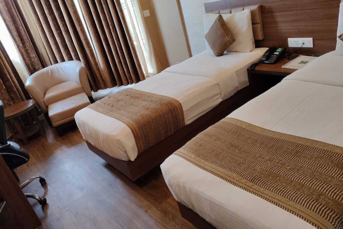 A hotel room with two beds, a chair, a bedside table, and a telephone.