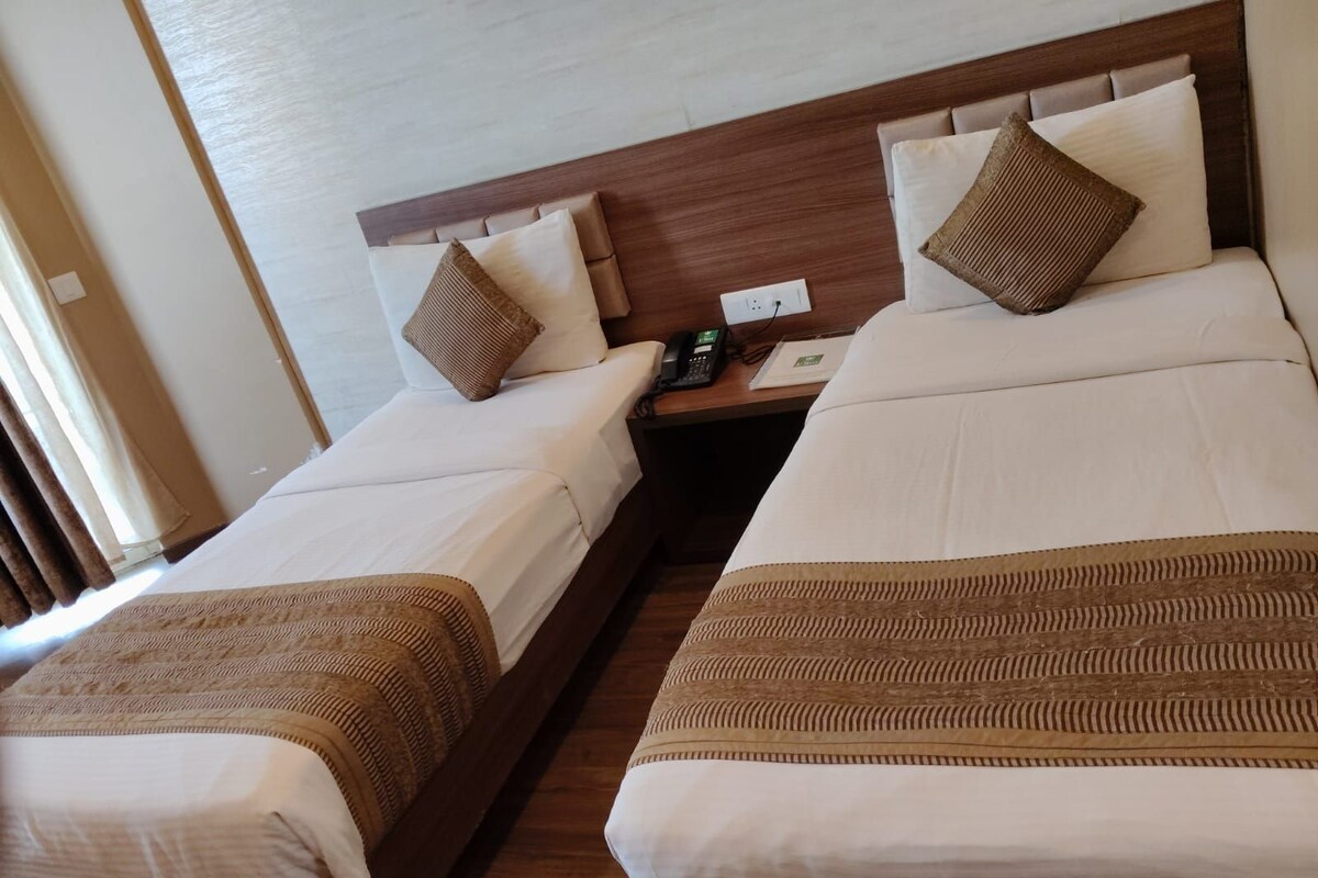 Une chambre d’hôtel avec deux lits simples, une tête de lit en bois, une table de chevet avec un téléphone et une fenêtre avec des rideaux.