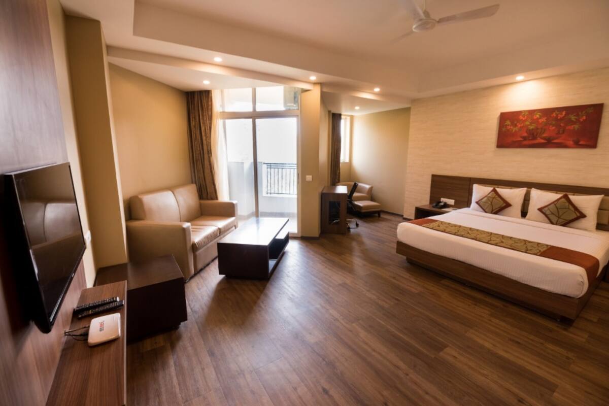 A hotel room with a bed, a sofa, a TV, a desk, and a balcony.