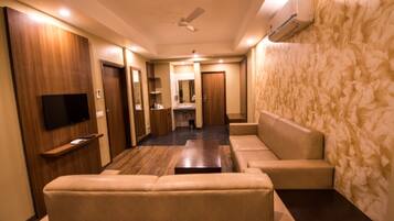 A hotel room with a sofa, a TV, a ceiling fan, and a wall-mounted air conditioner.