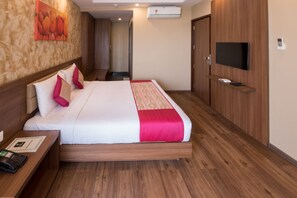 Habitación de hotel con cama, televisión, escritorio, teléfono y aire acondicionado.