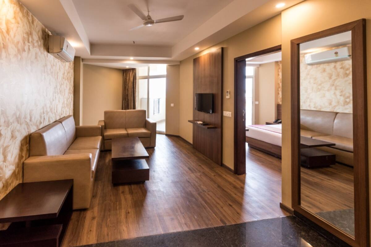 A modern hotel room with a sofa, a coffee table, a flat-screen TV, and a mirror.