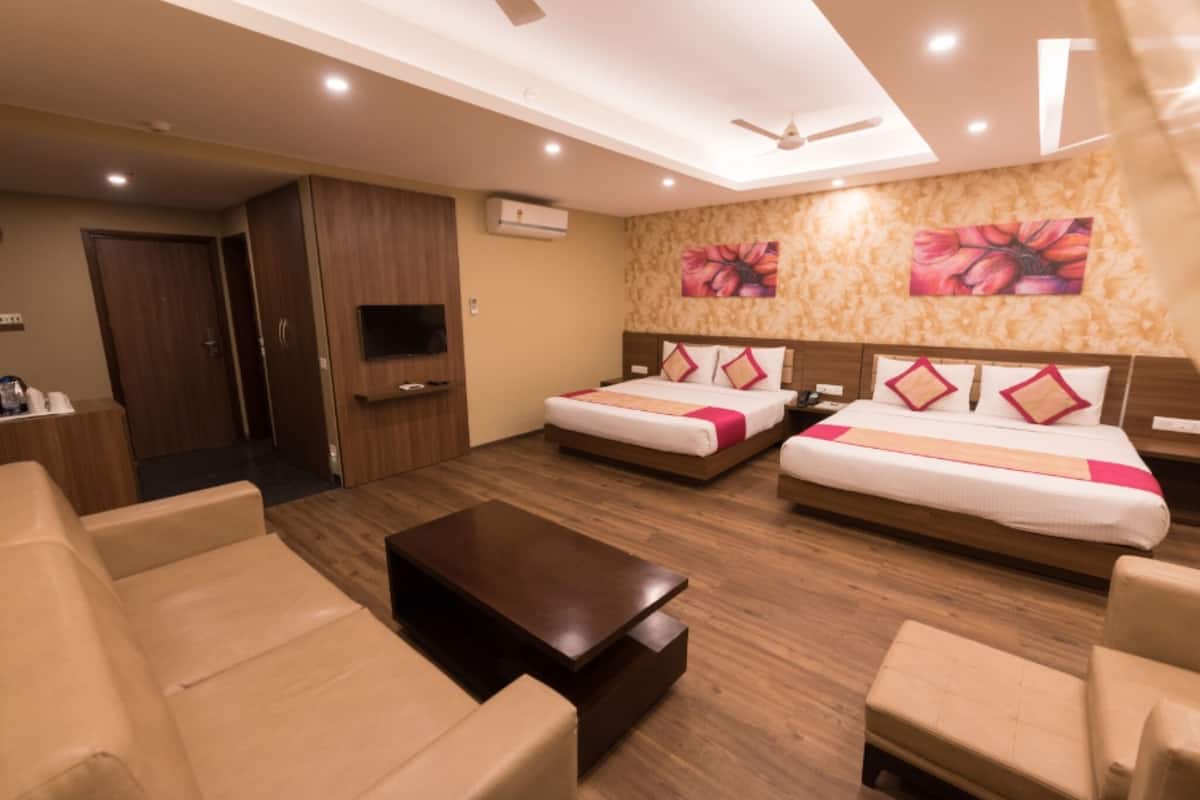 A hotel room with two beds, a sofa, a coffee table, a TV, and a ceiling fan.