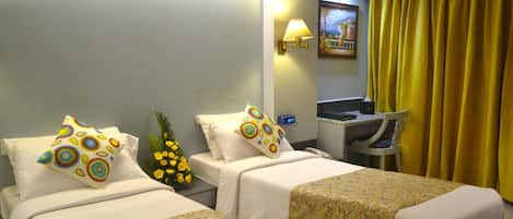 A hotel room with two beds, a desk, a lamp, and a painting on the wall.