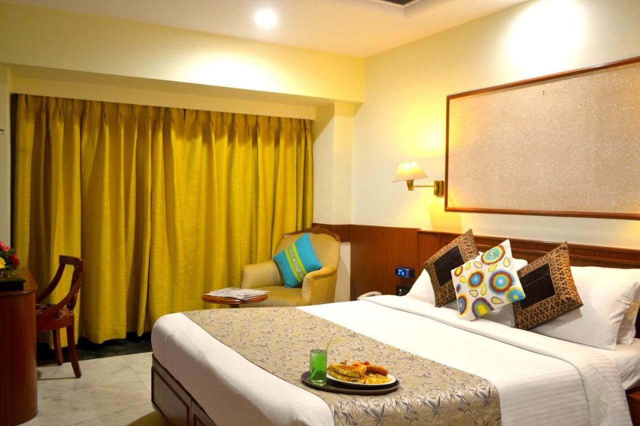 A hotel room with a bed, a chair, a table, and a curtain.