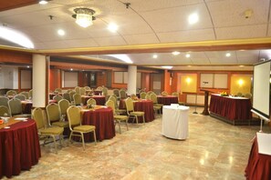 Una sala de banquetes amb taules rodones, cadirees i un escenari amb un micròfon.