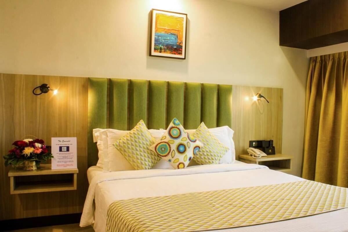 A hotel room with a bed, a nightstand with a phone, a framed picture on the wall, and a sign with room information.
