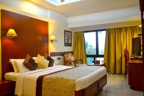 A hotel room with a large bed, two bedside lamps, a desk with a chair, a television, and a window with curtains. - Regenta Place The Emerald (Mumbai)