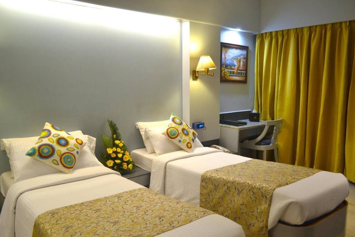 A hotel room with two beds, a desk, a lamp, and a painting on the wall.