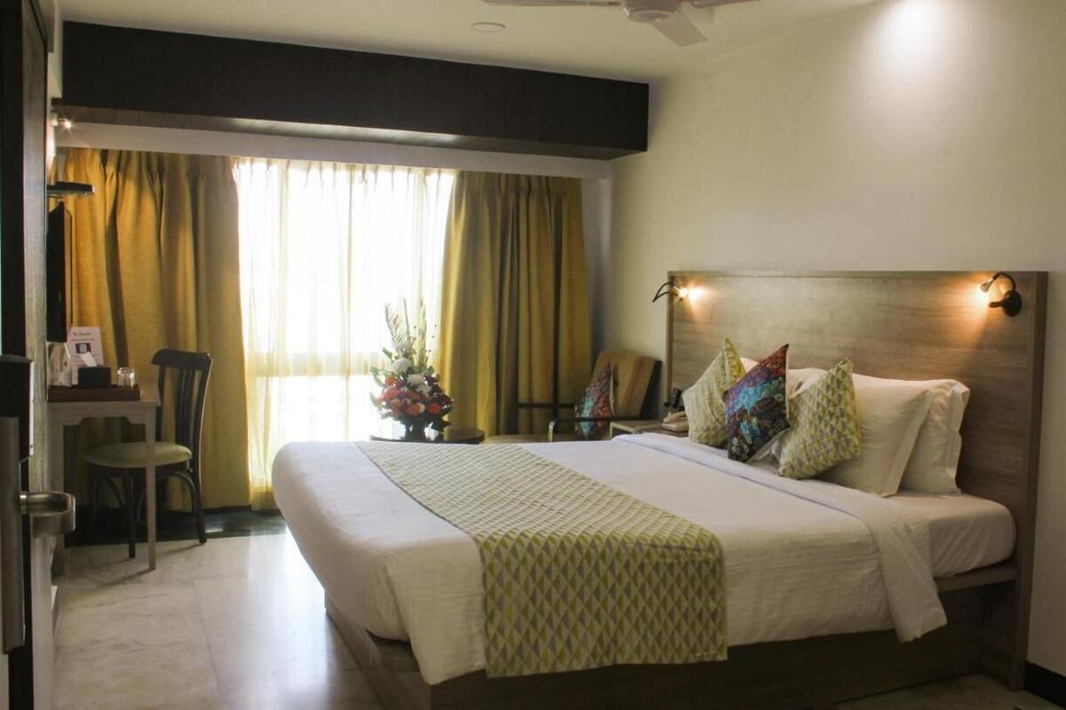 A hotel room with a bed, a desk, a chair, and a window with curtains.