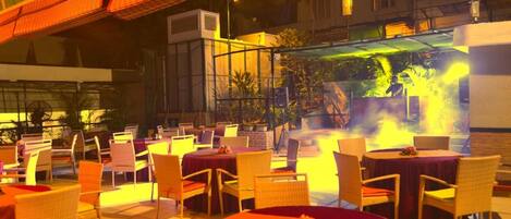 An outdoor dining area with tables and chairs, a fire feature, and a covered seating area.