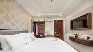 Ein Hotelzimmer mit einem großen Bett, einem Kleiderschrank, einem Schminktisch mit Spiegel und einem an der Wand befestigten Fernseher.
