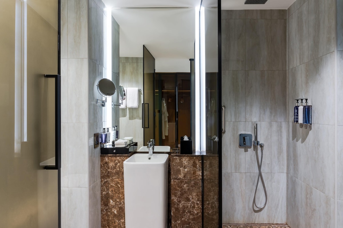 A modern bathroom with a sink, mirror, shower, and toiletries.