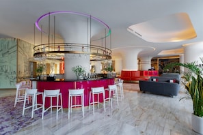 A modern bar area with a circular bar, white bar stools, and a vibrant red accent wall. - Voco Dubai Monaco Heart of Europe (Dubai)