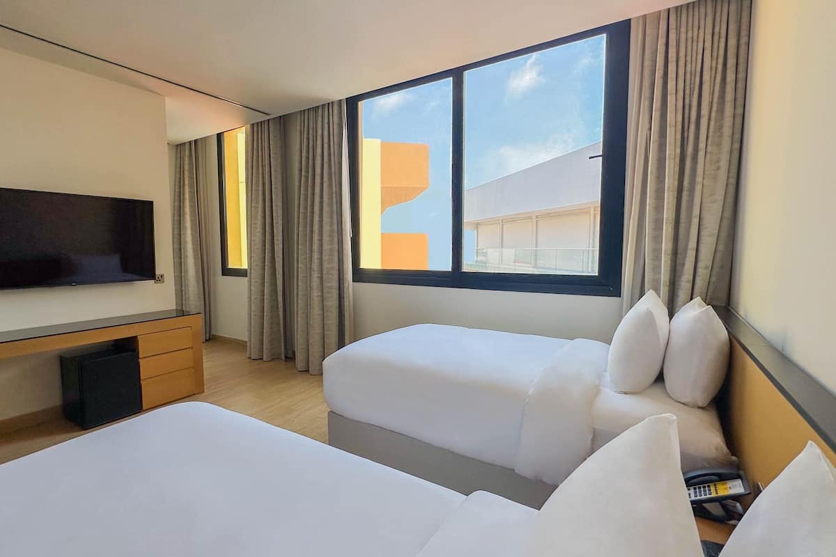 A hotel room with a TV, a desk, two beds, and a large window with curtains.