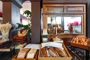 A bakery display with various breads and pastries, wooden crates, and a window view. - Voco Dubai Monaco Heart of Europe (Dubai)