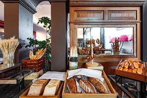 A bakery display with various breads and pastries, wooden crates, and a window view.