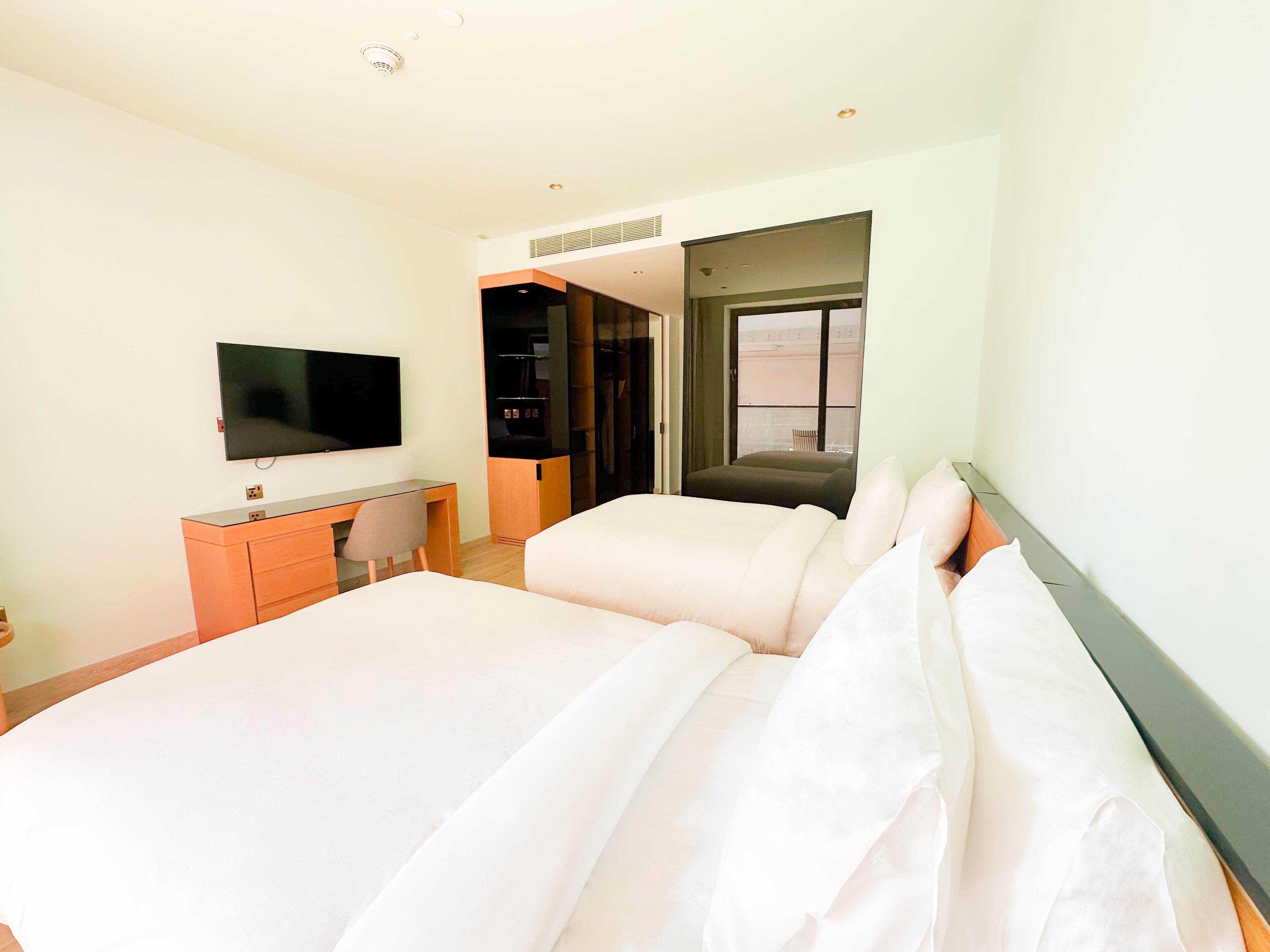 A hotel room with a bed, a desk, a chair, a TV, and a window.