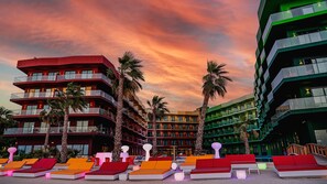 A hotel with multiple floors, outdoor seating areas, and palm trees. - Voco Dubai Monaco Heart of Europe (Dubai)