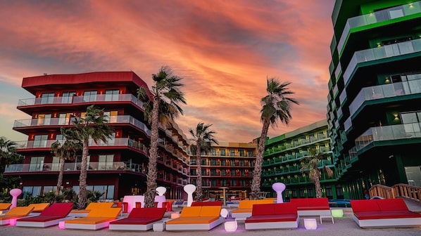 A hotel with multiple floors, outdoor seating areas, and palm trees. - Voco Dubai Monaco Heart of Europe (Dubai)