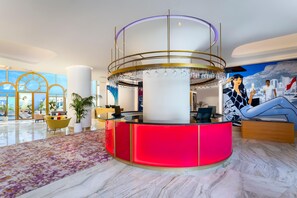 A modern lobby with a central reception desk, large windows, and a mural. - Voco Dubai Monaco Heart of Europe (Dubai)