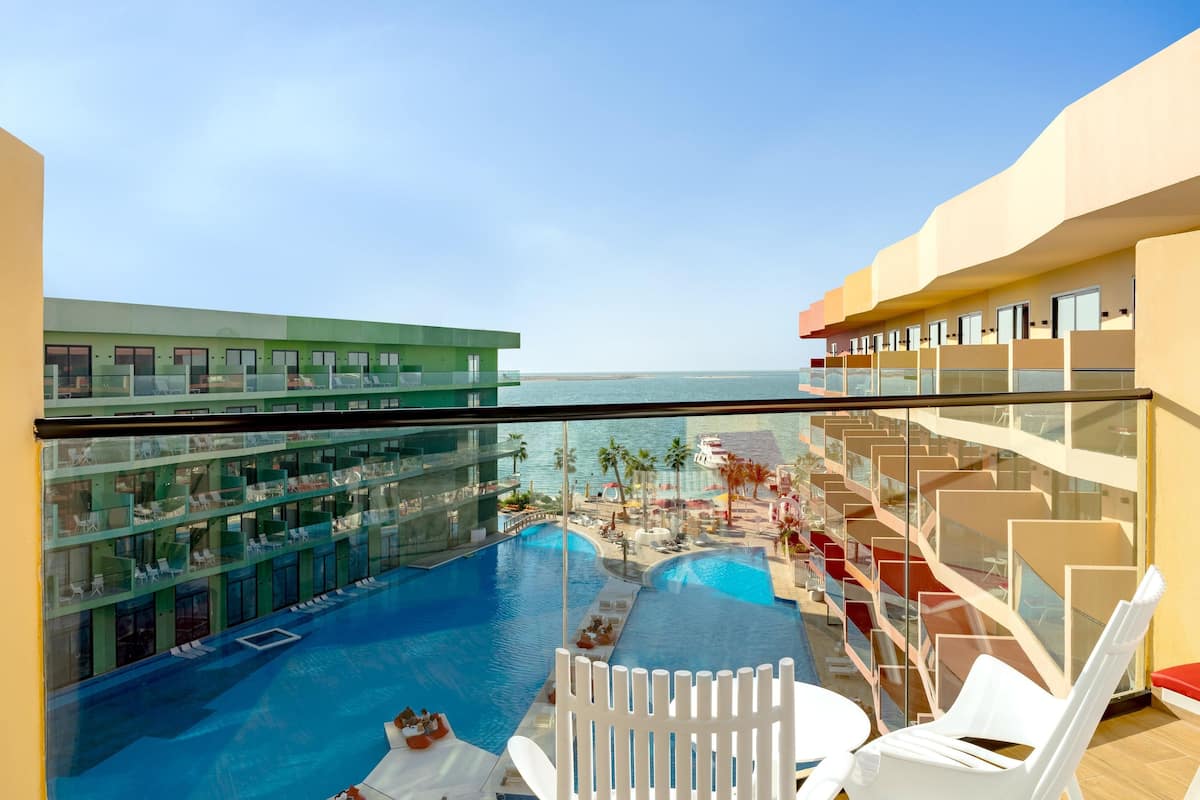 A hotel balcony with a pool, lounge chairs, and a view of the sea.