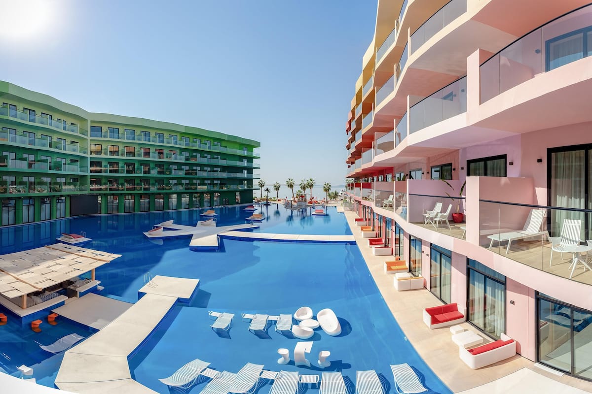 A modern hotel with a rooftop pool, multiple balconies, and a clear view of the sky.