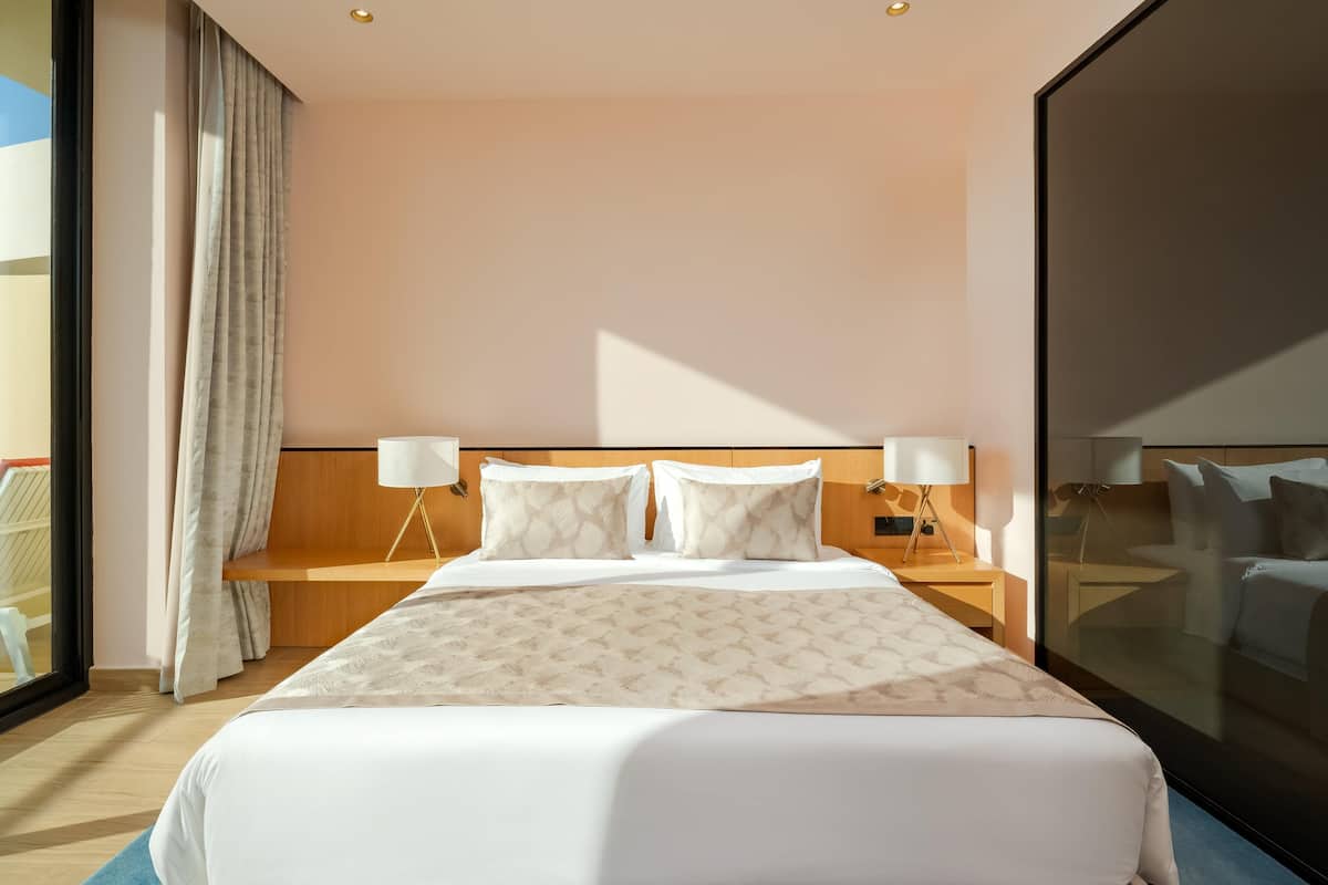 A hotel room with a large bed, two bedside tables, a window with curtains, and a view of the outside.