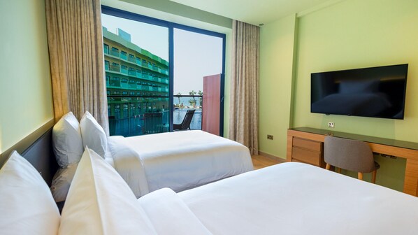 A hotel room with two beds, a TV, a desk, and a balcony with a view of a building and a pool. - Voco Dubai Monaco Heart of Europe (Dubai)