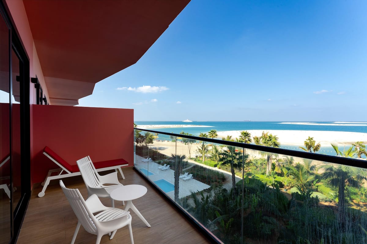 A balcony with white chairs and a table, overlooking a beach and palm trees.
