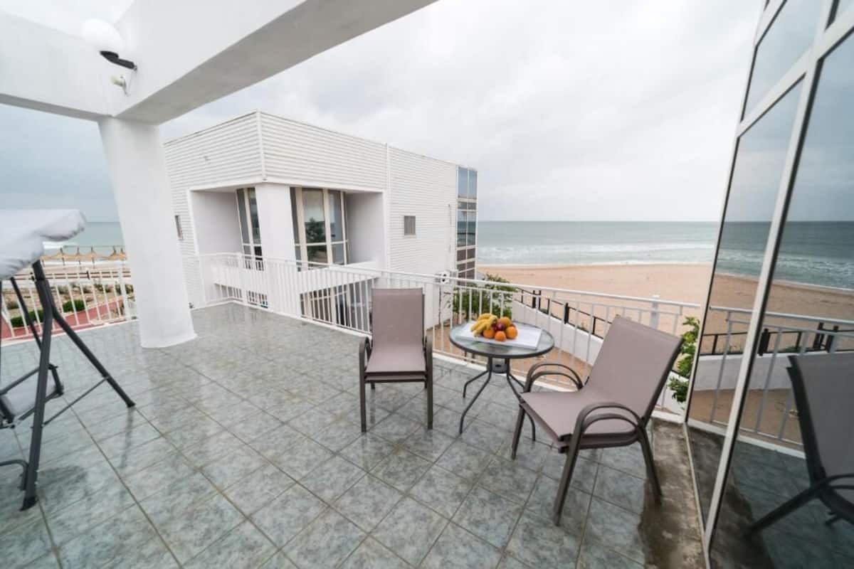 Un balcon avec une table et des chaises, un bâtiment blanc et une vue sur la plage.