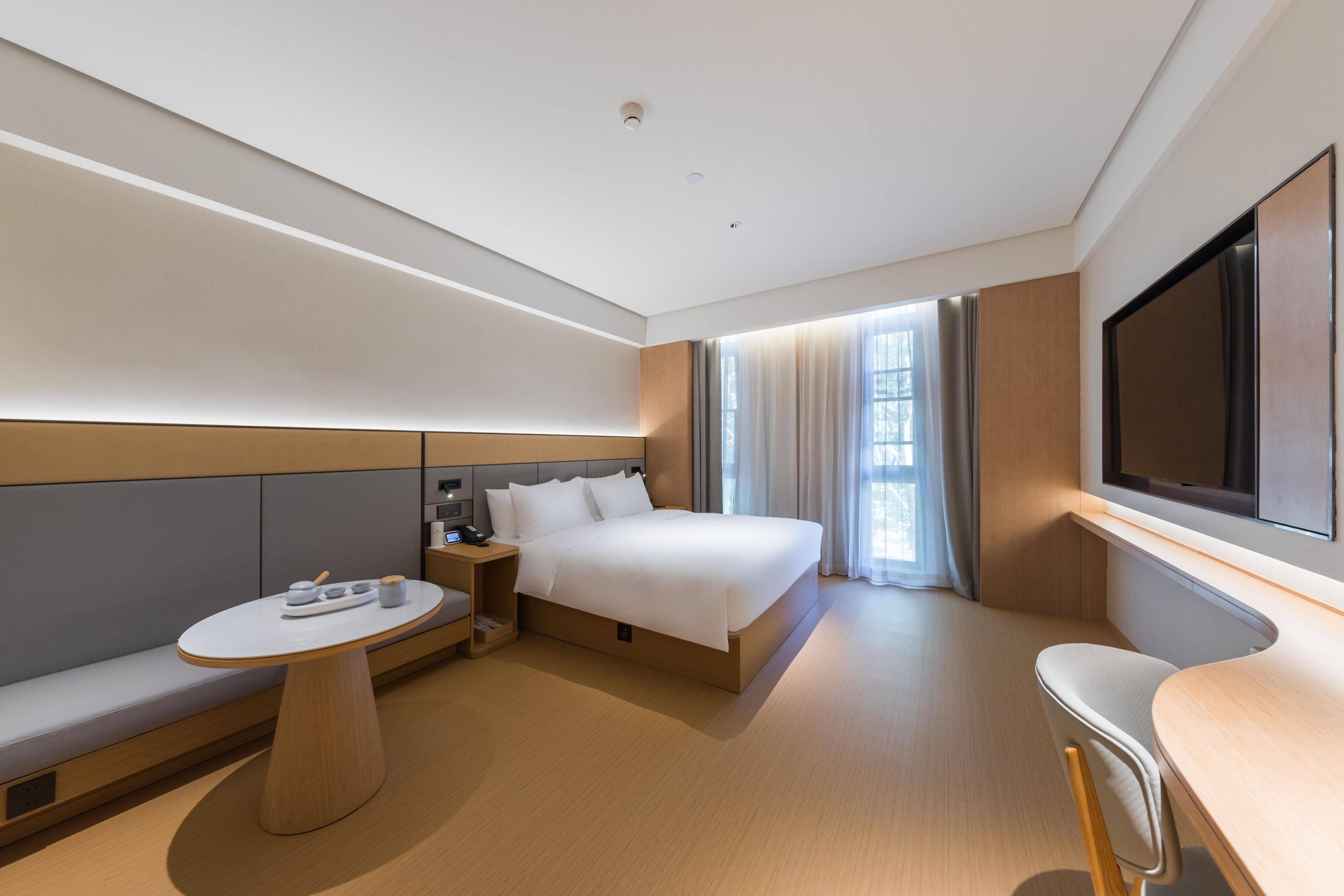 Une chambre d’hôtel moderne équipée d’un lit, d’une table de chevet, d’une chaise et d’un téléviseur fixé au mur.