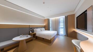 Une chambre d’hôtel moderne équipée d’un lit, d’une table de chevet, d’une chaise et d’un téléviseur fixé au mur.