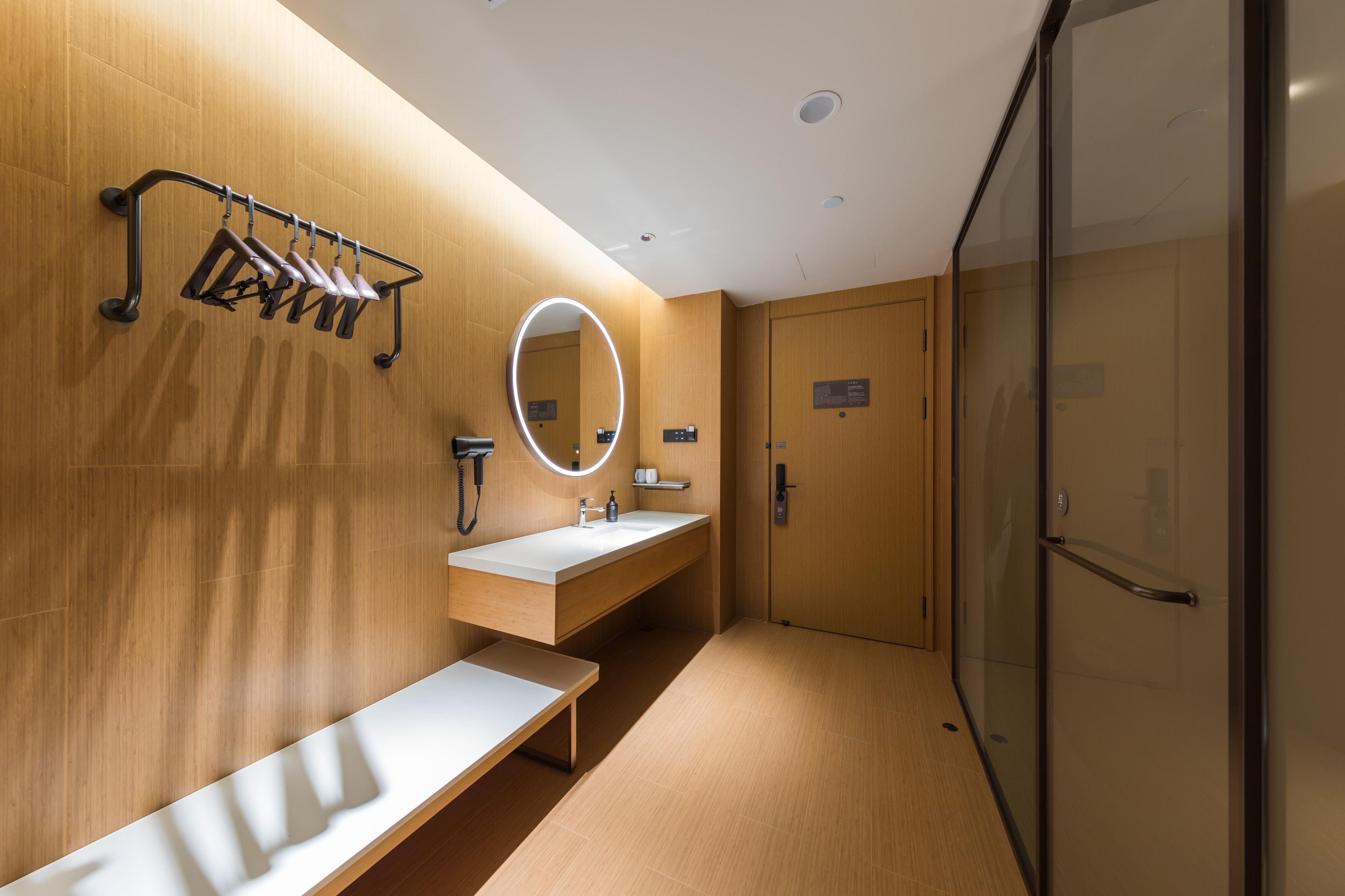 A modern bathroom with a wooden wall, a round mirror, a sink, and a bench.