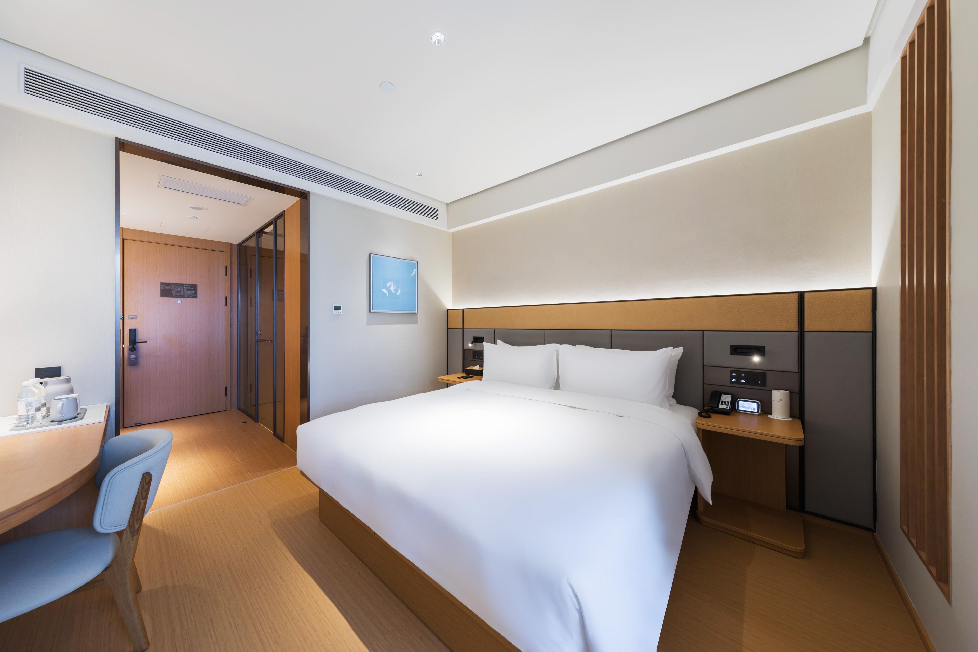 A hotel room with a bed, bedside table, chair, desk, and a door leading to another room.