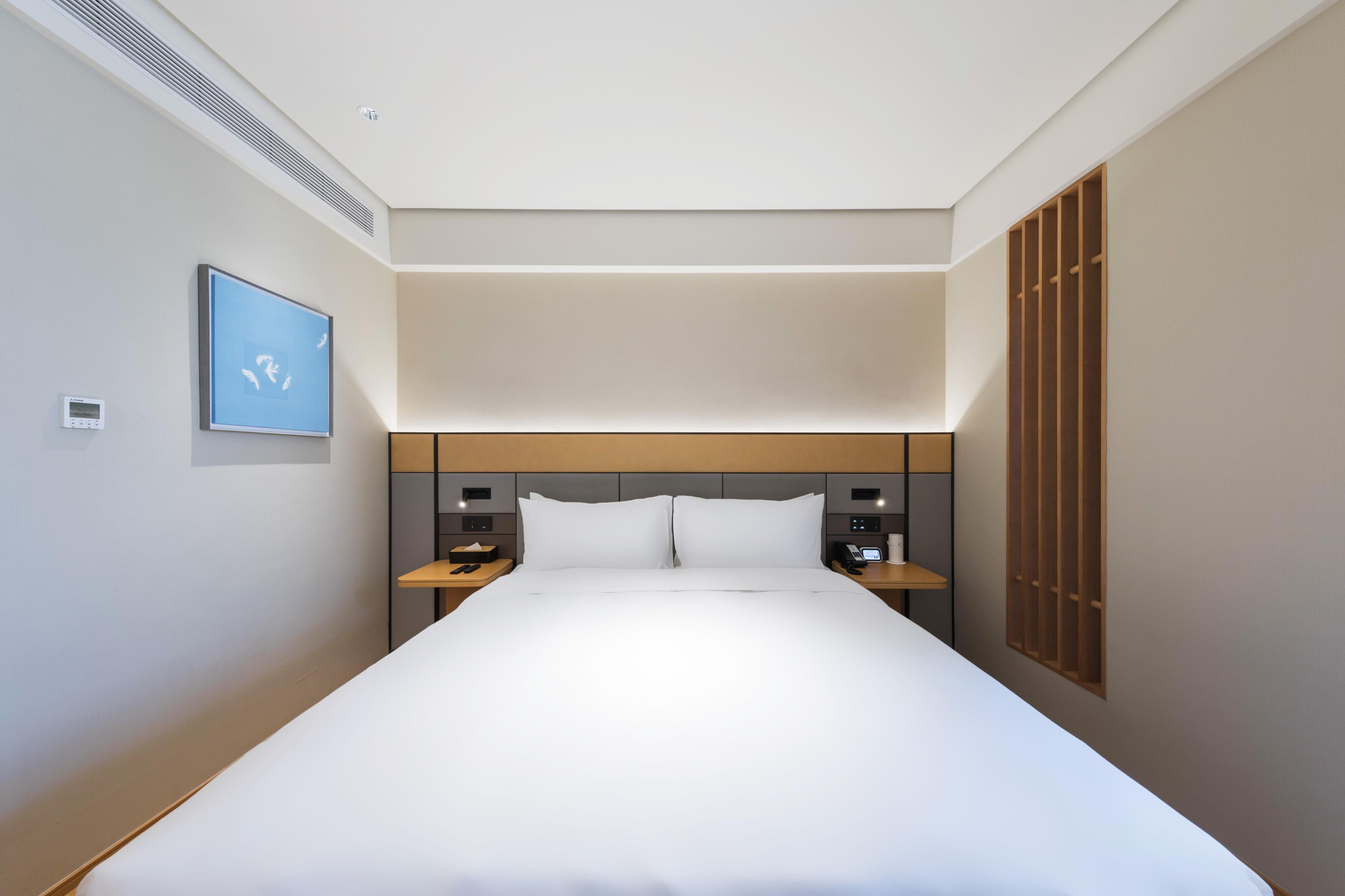 Una habitación de hotel moderna con una cama grande, mesitas de noche, un televisor de pared y una ventana con persianas.