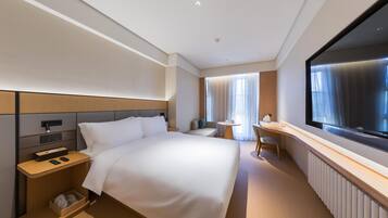 Een moderne hotelkamer met een groot bed, nachtkastje, televisie en een klein bureau.