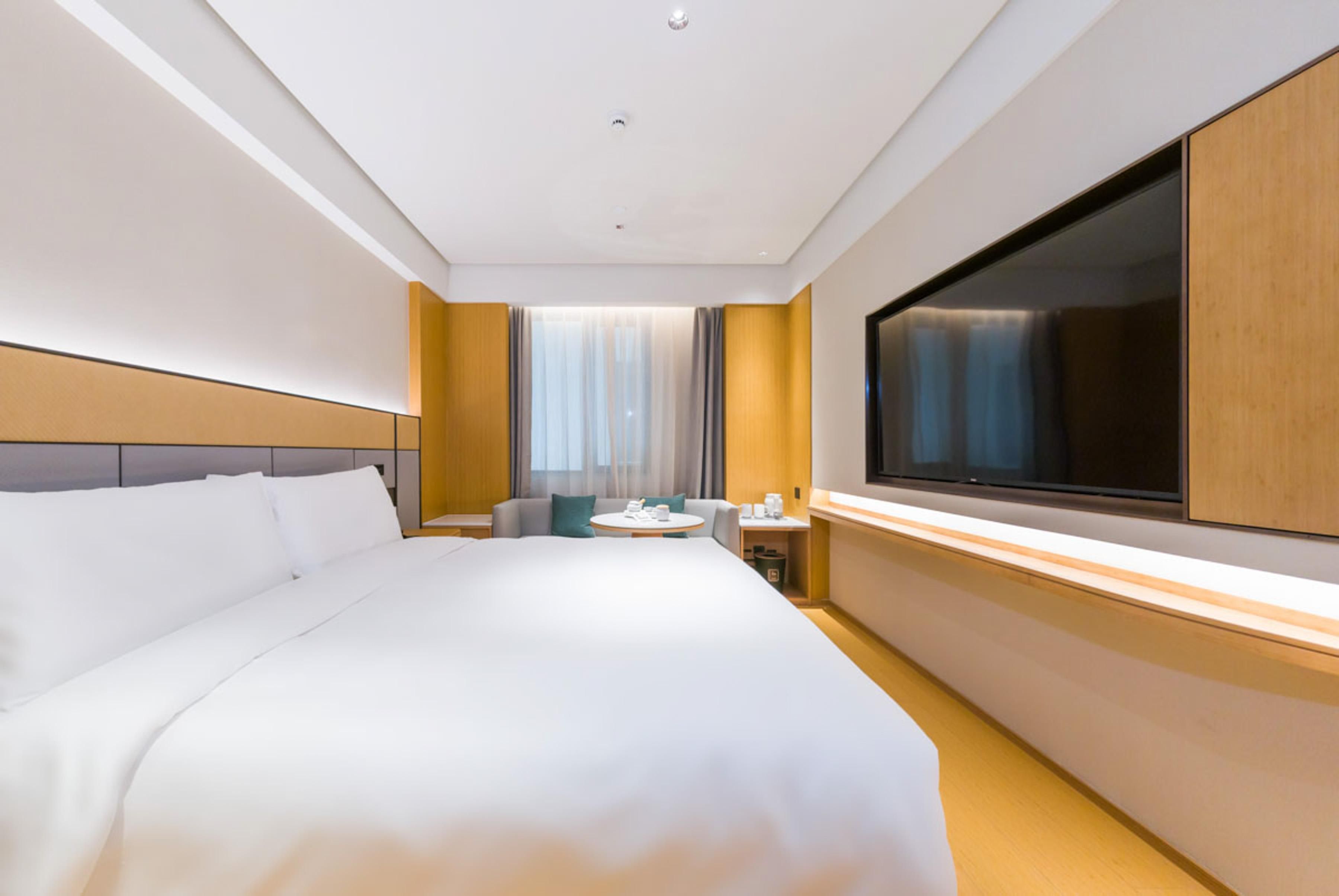 A hotel room with a large bed, a TV, a small round table, and a window with curtains.