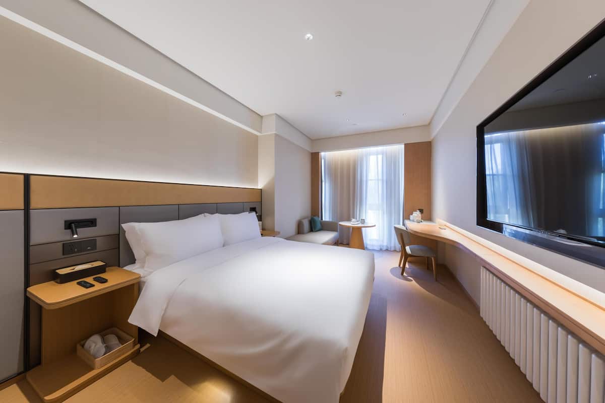 Ein modernes Hotelzimmer mit einem großen Bett, Nachttisch, Fernseher und einer kleinen Schreibtischzeile.