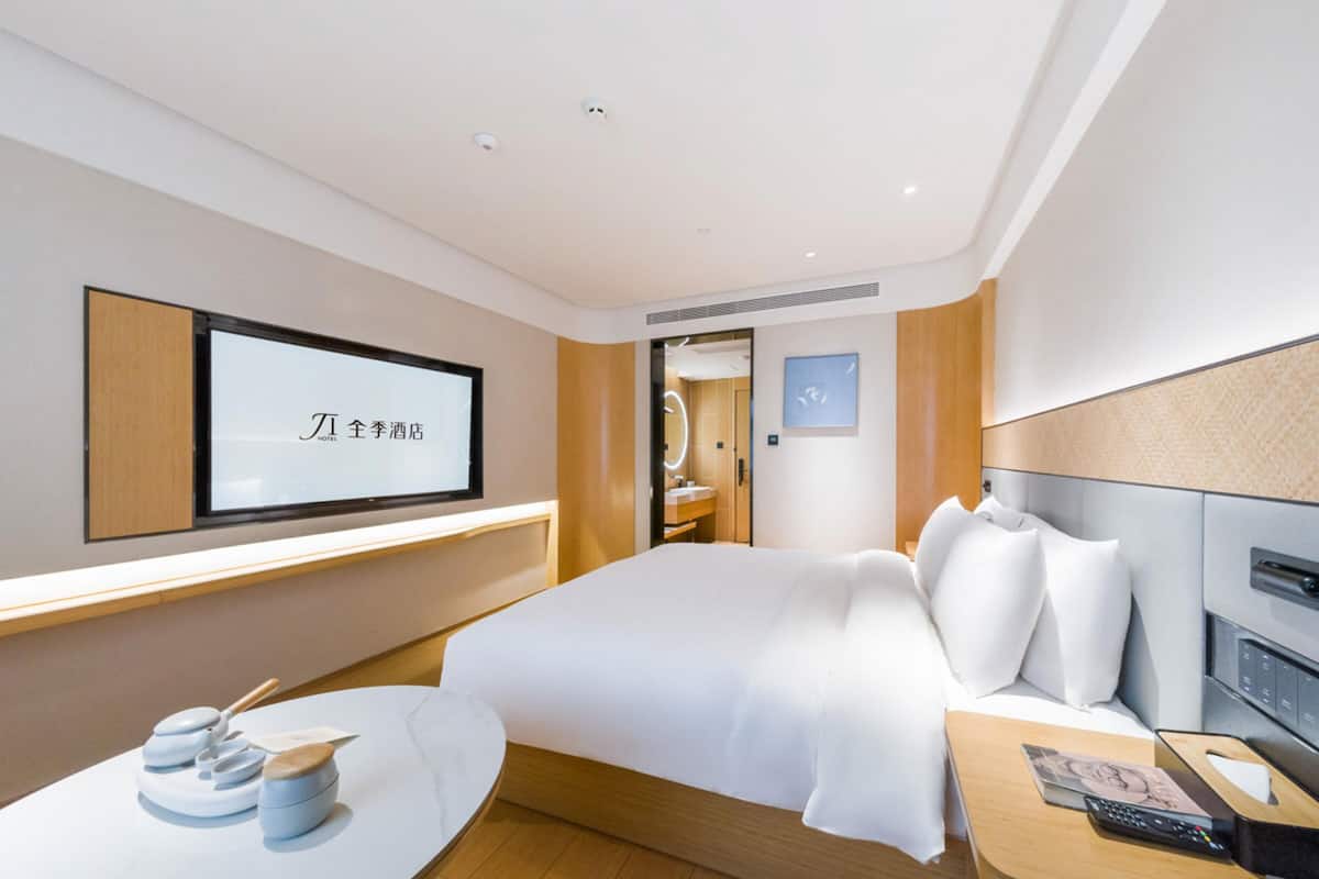 Ein modernes Hotelzimmer mit einem großen Bett, einem Nachttisch und einem an der Wand befestigten Fernseher.