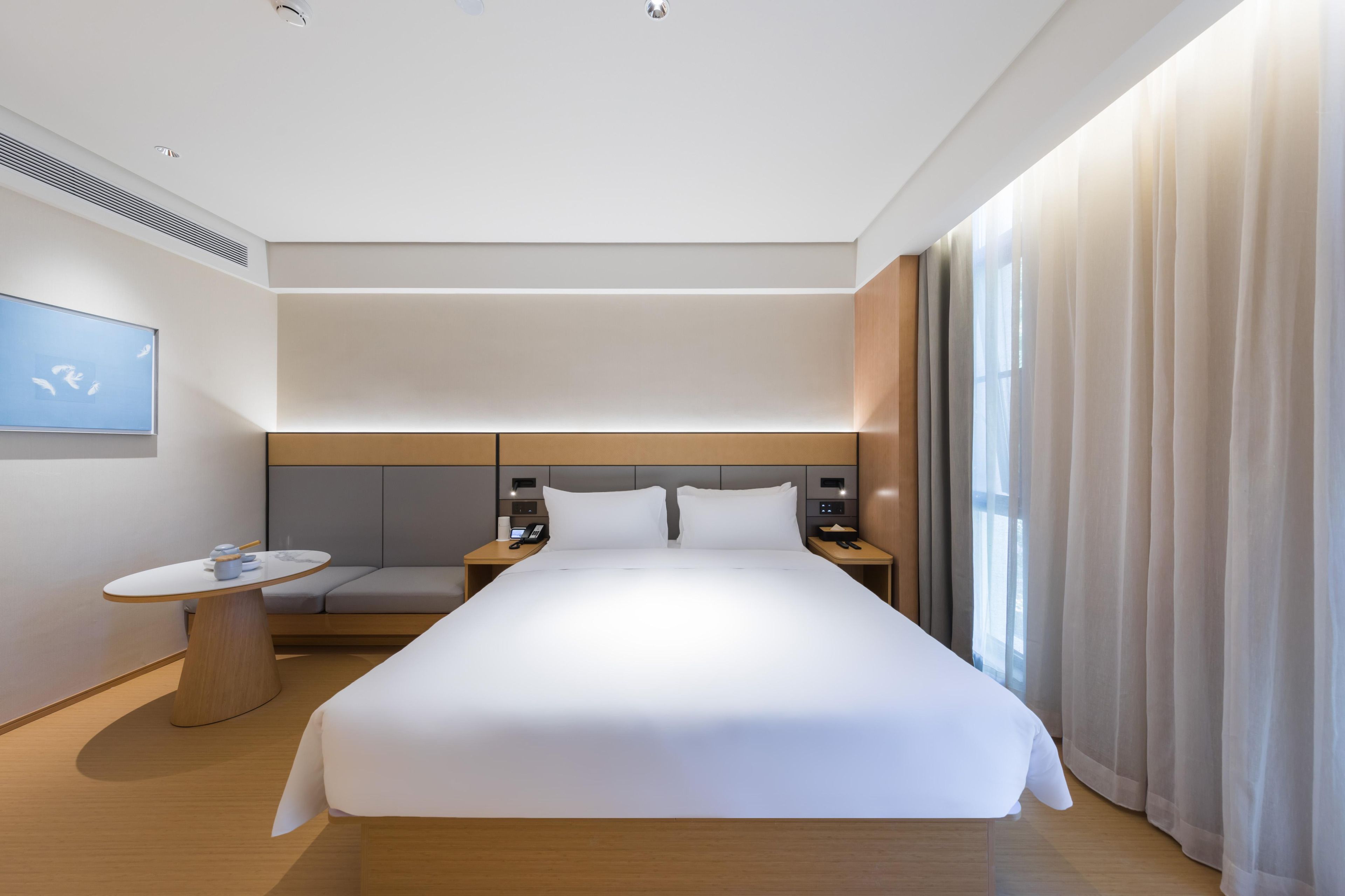 Habitación de hotel moderna con una cama grande, mesitas de noche, una pequeña mesa redonda y vistas al exterior.