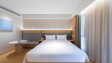 Habitación de hotel moderna con una cama grande, mesitas de noche, una pequeña mesa redonda y vistas al exterior.