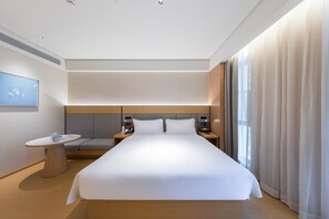 Ein modernes Hotelzimmer mit einem großen Bett, Nachttischen, einem kleinen runden Tisch und Blick ins Freie.