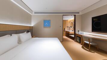 Habitación de hotel con una cama grande, un escritorio, un televisor y un baño visible a través de una puerta abierta.