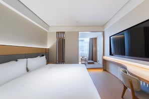 Quarto de hotel com uma cama grande, uma escrivaninha com cadeira, televisão e vista para o exterior.