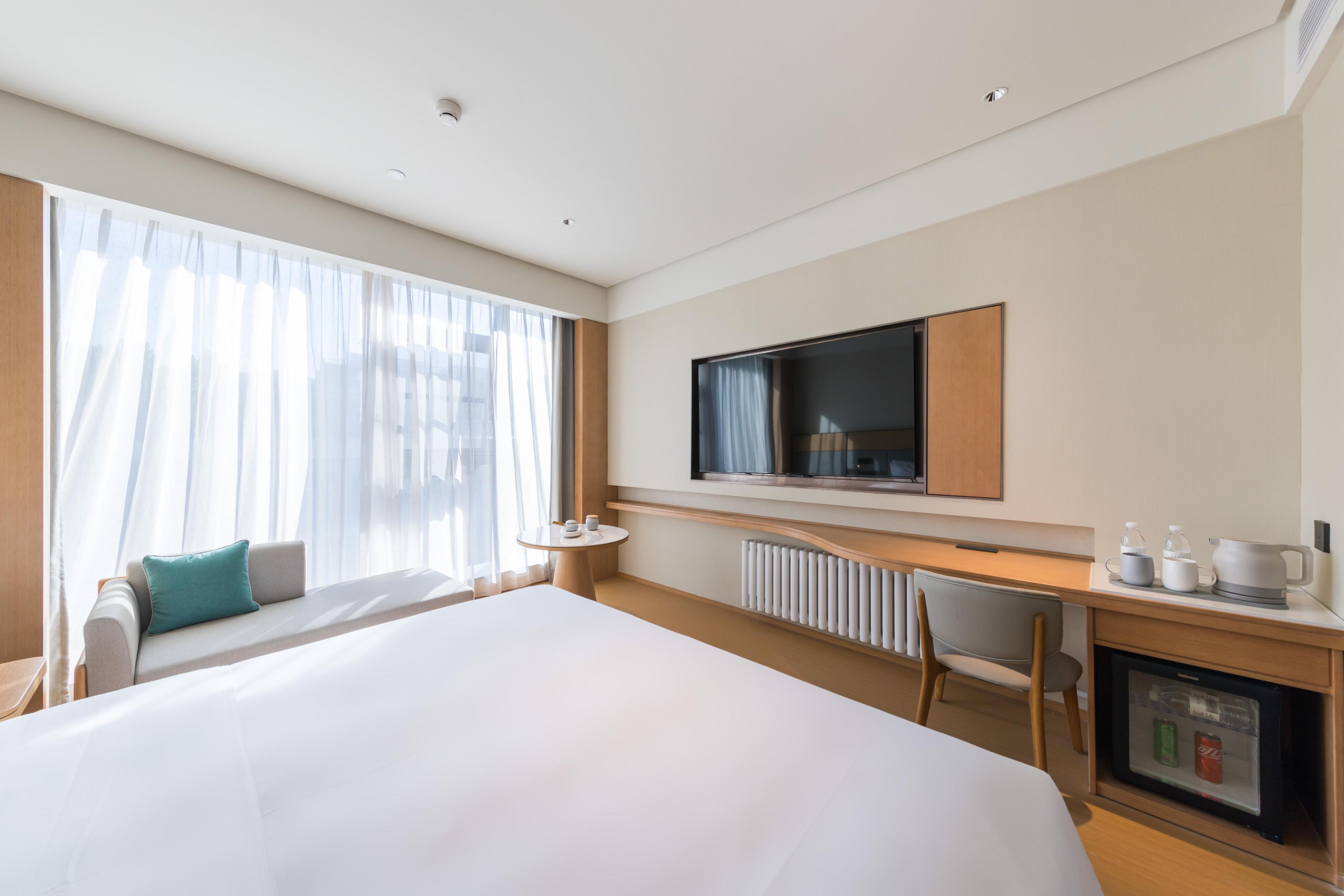 A hotel room with a large bed, a desk, a chair, a television, and a minibar.