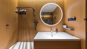 A modern bathroom with a wooden wall, a round mirror with a light, a white sink, a towel rack, and a cup holder. - Ji Hotel Beijing Beiqing Road Zhongguancun Environ (Beijing)