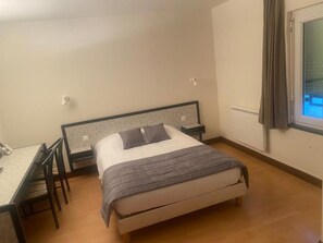 Un dormitorio con cama, mesita de noche, silla y ventana con cortinas.